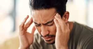 A close-up view shows a man with his hands on his temple. He has his eyes closed and a distressed look on his face.