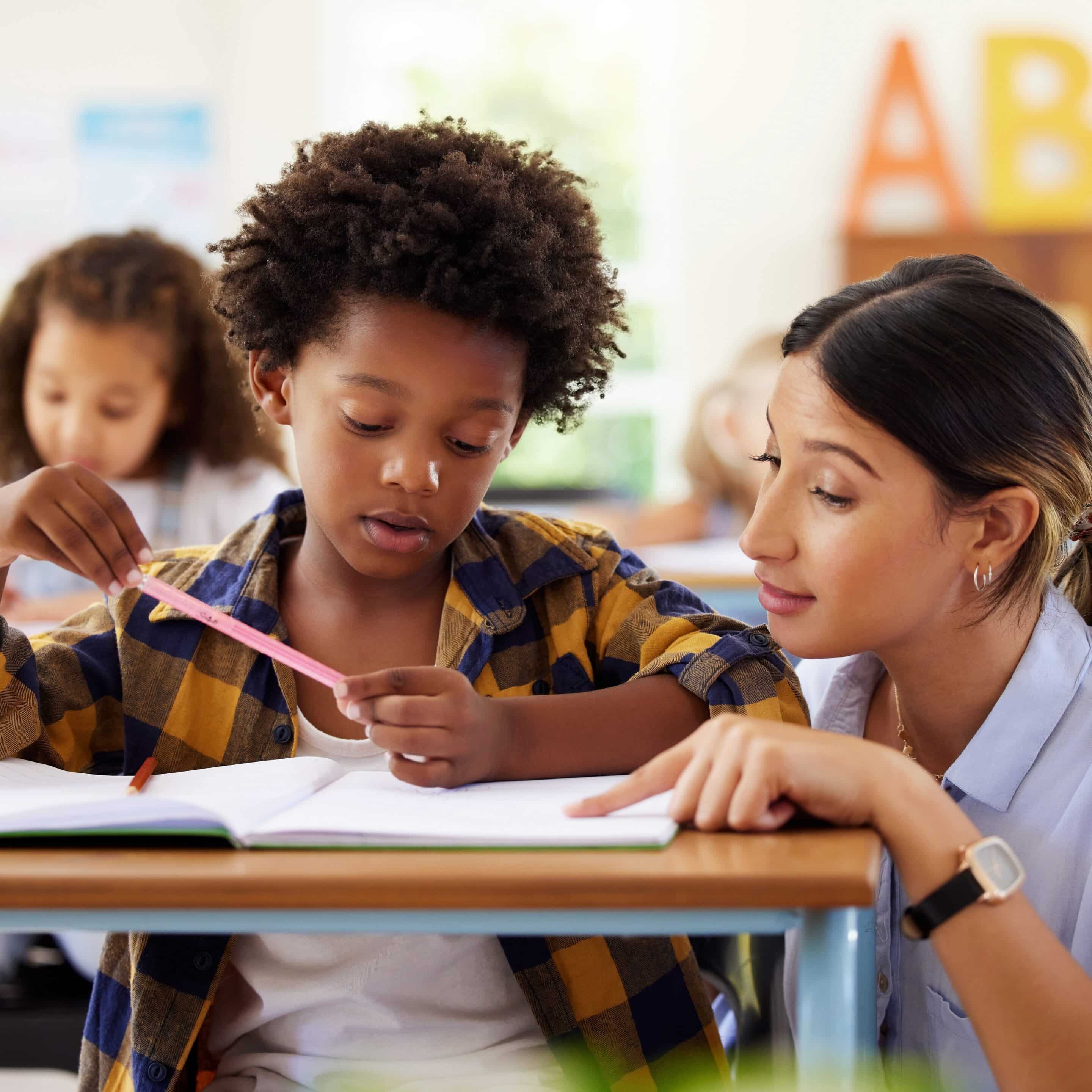 Classroom Kit (Cover Image) Photo of teacher working with a student at his desk in a classroom